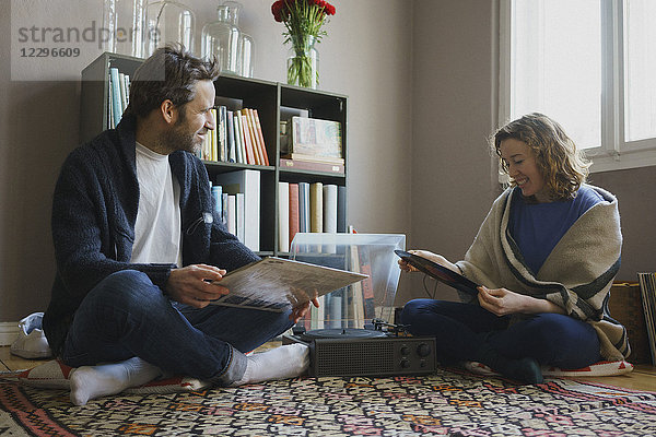 Fröhliches mittleres erwachsenes Paar sitzend mit Plattenteller auf Teppich zu Hause