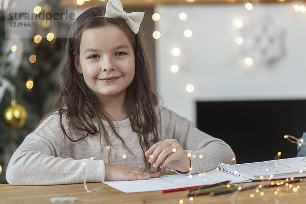 Porträt eines lächelnden Mädchens am Tisch sitzend mit beleuchteten Lichterketten