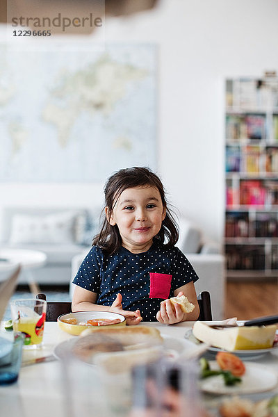 Portrait of cute smiling girl having breakfast at table in house