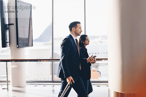 Side view of businessman and businesswoman walking in airport terminal