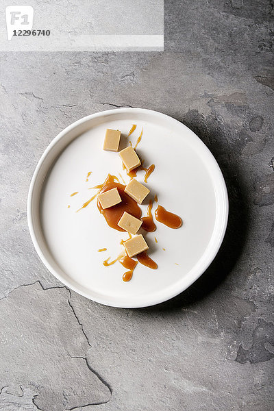 Gesalzene Karamellbonbons mit Karamellsoße in weißem Teller über grauem Texturhintergrund