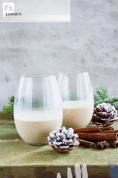 Gläser mit traditionellem Winter-Eierlikör mit Milch  Rum und Zimt  weihnachtliche Dekoration auf Holztisch