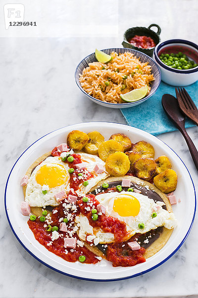 Huevos Motuleños (Spiegeleier auf einer Tortilla mit schwarzem Bohnenpüree  Chilisauce  Kochbananen  Speck und Käse  Mexiko)