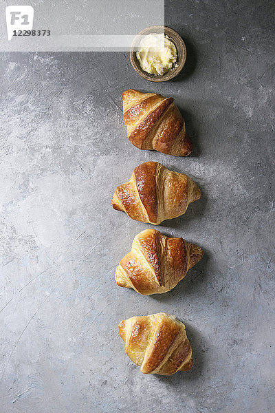 Frisch gebackenes traditionelles Croissant mit Butter in Reihe über grauer Textur Hintergrund