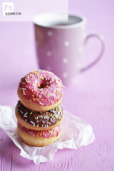 Ein Stapel von drei Mini-Doughnuts mit Zuckerguss und Zuckerfäden vor einer Teetasse