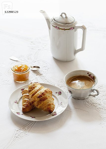 Croissants  ein Glas Aprikosenmarmelade  eine Tasse Kaffee und ein Kännchen Kaffee