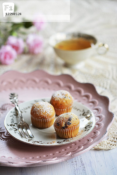 Kleine Muffins auf einem Teller mit einer Gabel  einer Teetasse und Blumen
