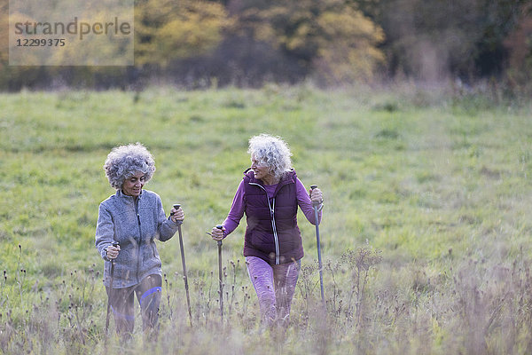 Active senior women friends hiking with poles up rural hillside