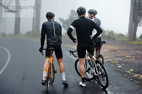 Male cyclist friends taking a break  resting on wet road