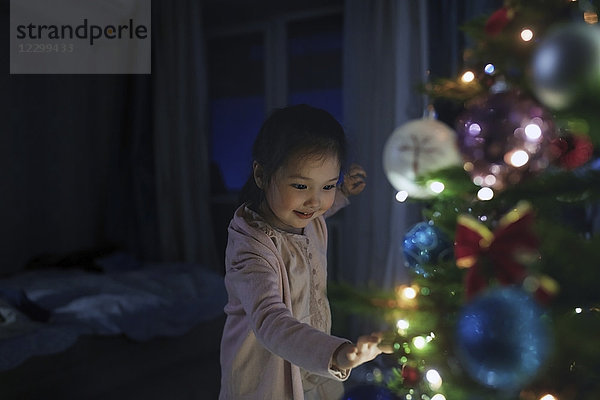 Curious  cute girl touching illuminated Christmas tree