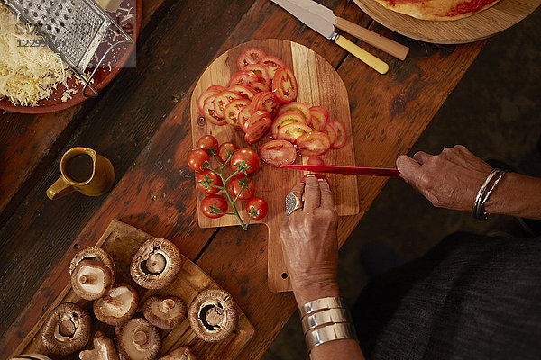 Overhead view woman slicing fresh tomatoes for pizza