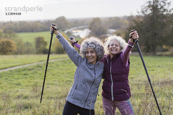 Portrait enthusiastic  confident active senior women friends hiking with poles in rural field