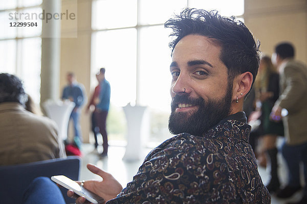 Portrait smiling businessman with beard using smart phone in conference audience