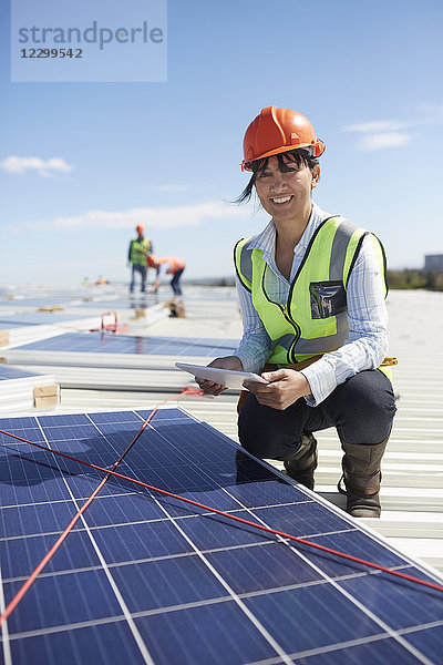 Portrait confident  smiling female engineer with digital tablet examining solar panels at power plant