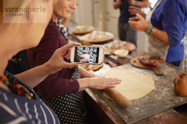 Woman with camera phone photographing friend making pizza dough in cooking class