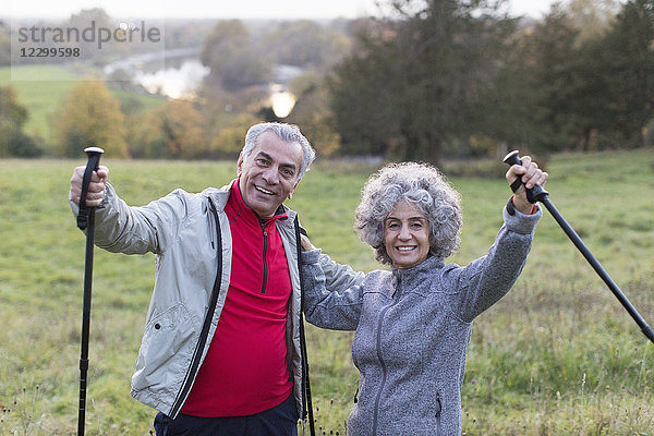 Portrait enthusiastic  confident active senior couple hiking with poles in rural field