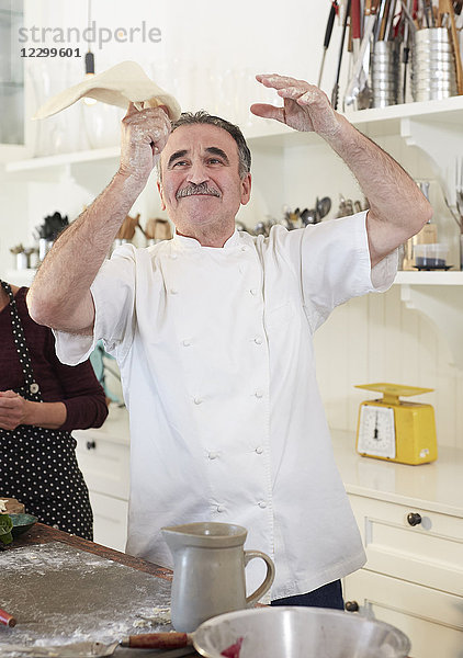 Playful senior chef tossing pizza dough in kitchen