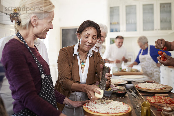 Senior women friends grating cheese over pizza in cooking class