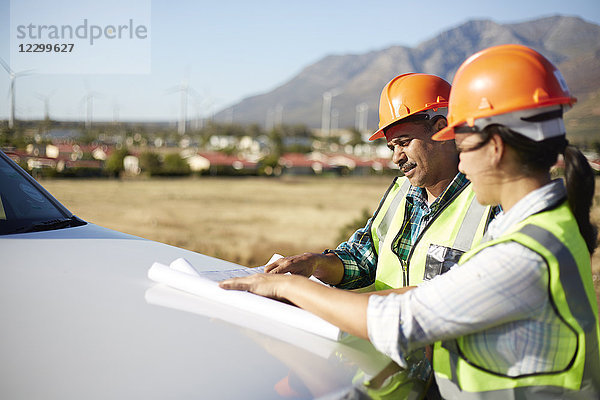 Engineers reviewing blueprints at truck at sunny power plant