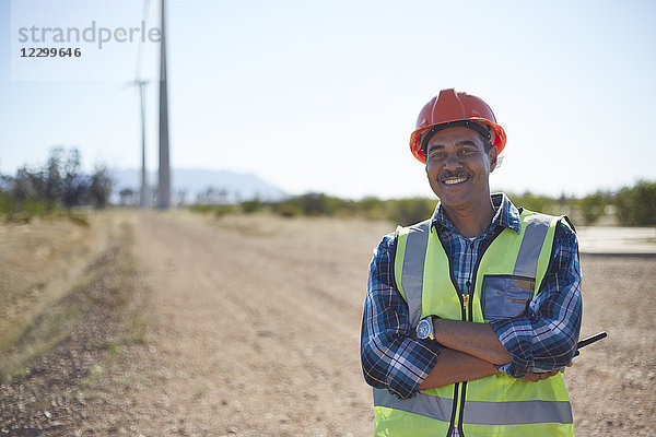 Portrait smiling engineer on dirt road at wind turbine power plant