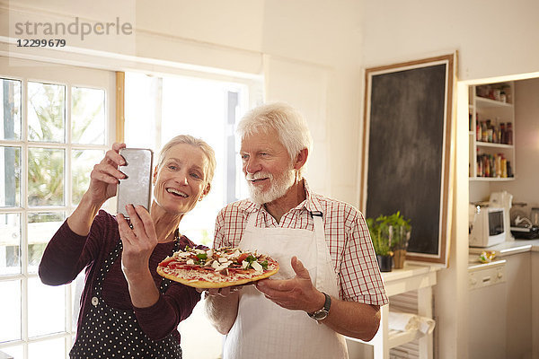 Smiling  confident senior couple taking selfie with pizza at cooking class