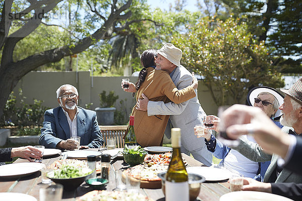 Friends toasting affectionate senior couple hugging at sunny garden party