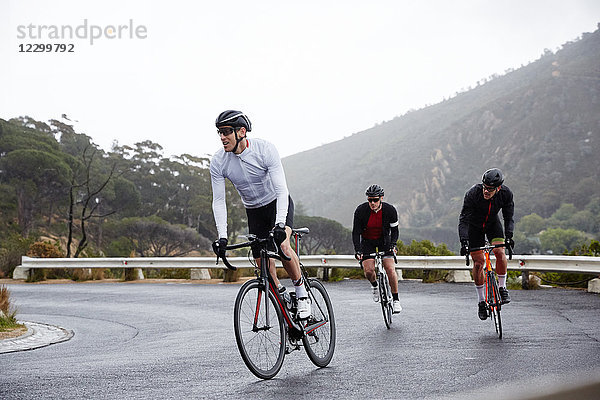 Male cyclists cycling uphill on wet road