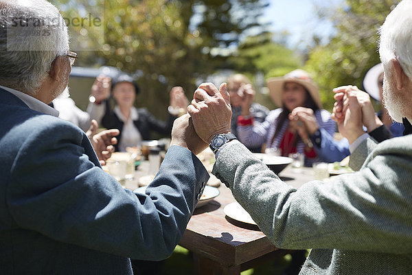 Active senior friends holding hands  praying at sunny garden party table