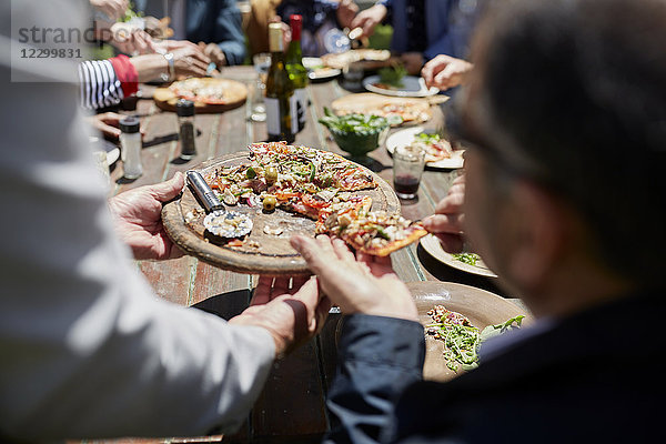Friends sharing homemade pizza at sunny patio table
