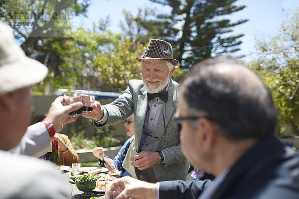 Senior man in suit and bow tie toasting friends with wine at sunny garden party