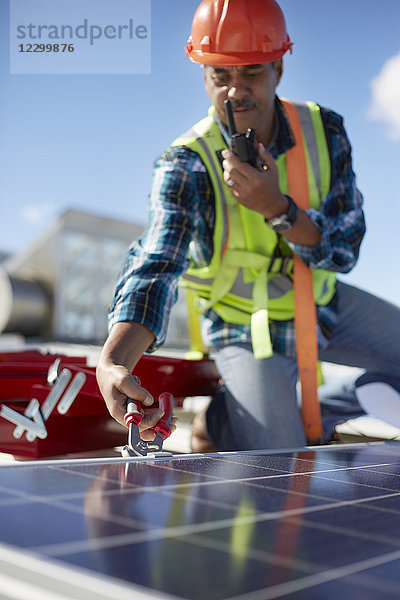 Male engineer with walkie-talkie repairing solar panel at power plant