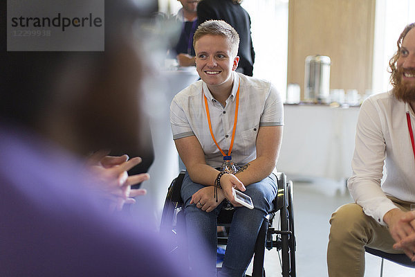 Smiling woman in wheelchair talking to colleagues in conference