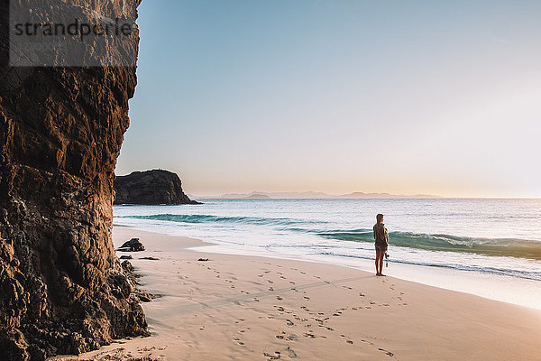Seitenansicht einer Frau  die den Sonnenuntergang am leeren weißen Sandstrand beobachtet  Lanzarote  Kanarische Inseln  Spanien