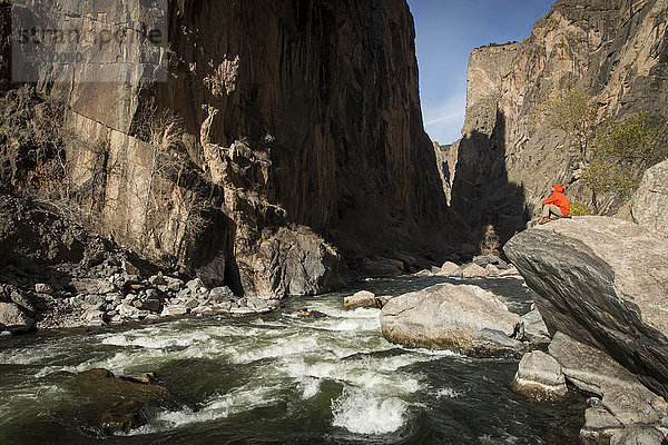 Wanderer sitzt auf einem Felsen über dem Fluss am Grund des Black Canyon  Colorado  USA