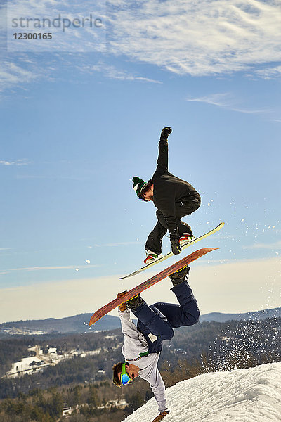 Ein Snowboarder überfliegt einen anderen bei einem Handplant im Terrain Park.