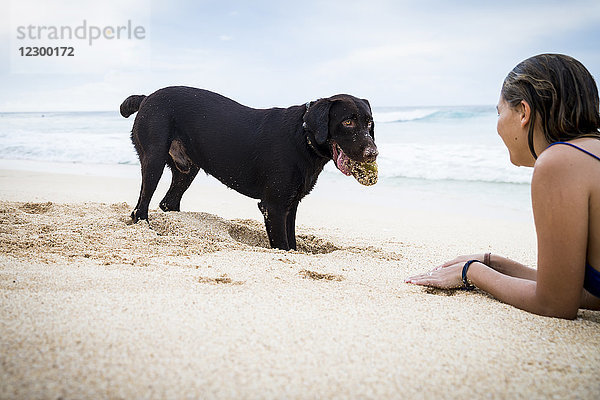 Frau spielt zusammen mit Hund am Strand