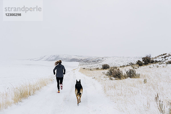 Eine junge Sportlerin und ihr Hund laufen an einem nebligen Wintermorgen einen Trail.