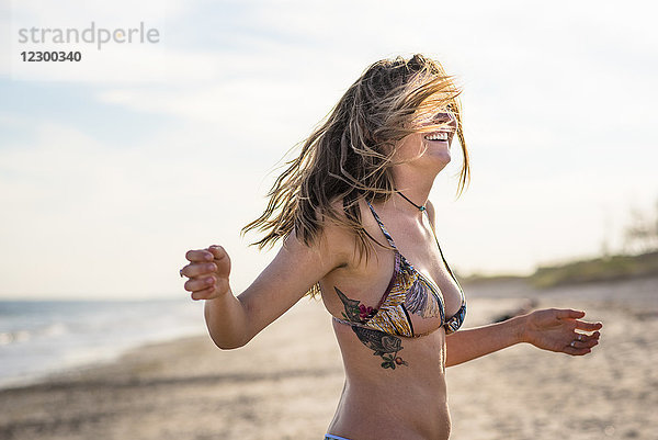 Taillenaufnahme einer jungen lächelnden Frau im Bikini am Strand