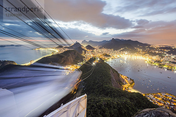 Unscharfe Spur einer Seilbahn  die sich gegen die beleuchtete Küstenstadt in der Abenddämmerung bewegt  Rio de Janeiro  Brasilien