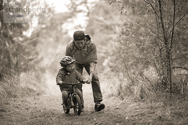 Frontansicht eines Vaters  der seinem Sohn hilft  ein kleines Fahrrad zu fahren  Rancho Santa Elena  Hidalgo  Mexiko