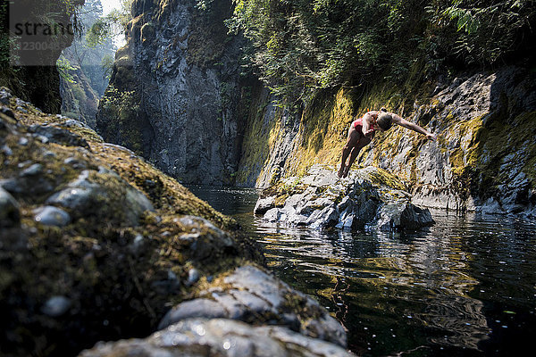 Frau im Bikini taucht von einem Felsen ins Wasser