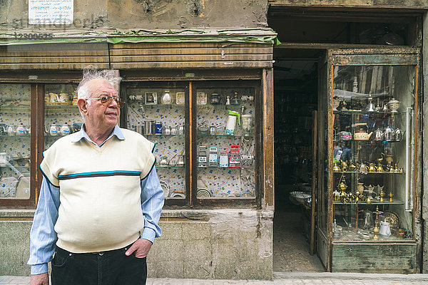 Porträt eines älteren Mannes  der mit der Hand in der Tasche vor einem Second-Hand-Laden steht  Alexandria  Ägypten