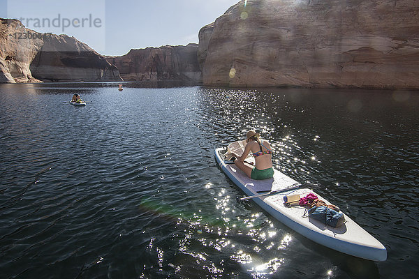 Rückansicht einer Frau  die auf einem Stand-up-Paddleboard sitzend auf eine Karte schaut  Lake Powell  Utah  USA