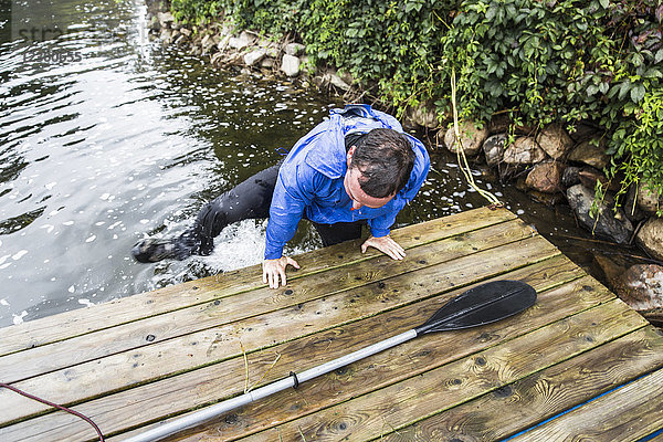 Mann klettert aus dem Wasser auf den Steg  nachdem er aus dem Kajak gefallen ist