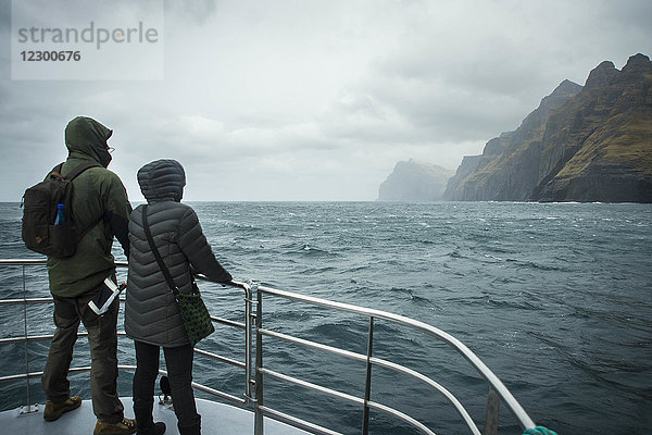 Touristenpaar mit Blick auf die Küste der Färöer Inseln vom Schiff aus