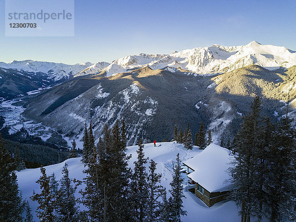 Luftaufnahme eines Bergtals und einer Person  die neben einer isolierten Hütte auf dem Gipfel eines schneebedeckten Berges steht  Aspen  Colorado  USA