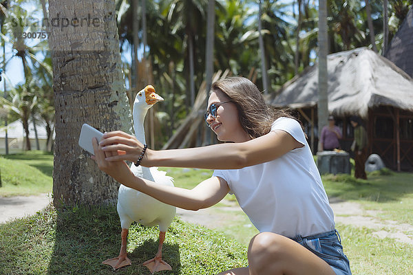 Junge Frau mit blauer Sonnenbrille macht ein Selfie mit Gans