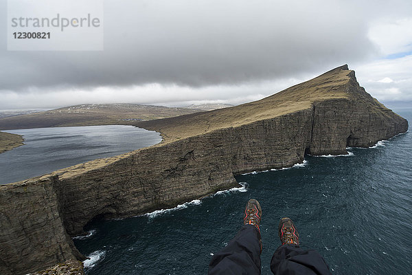 Wanderer  die mit den Füßen über den Rand einer Meeresklippe ragen  Färöer Inseln