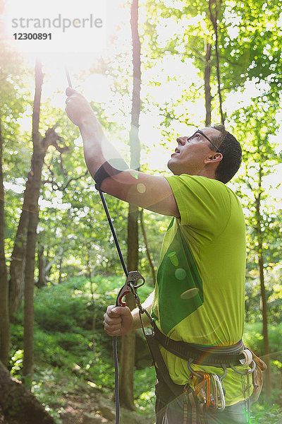 Ein Mann mittleren Alters beobachtet an einem warmen Herbstnachmittag einen Kletterer beim Aufstieg  während er sichert.