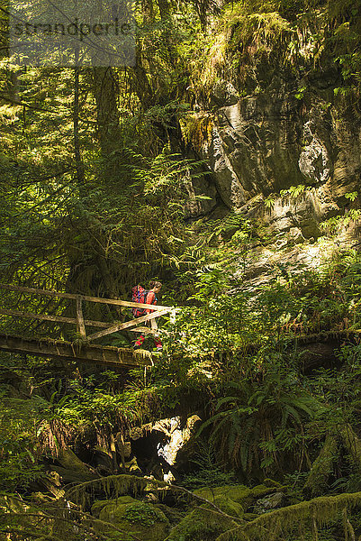 Eine mittelgroße Frau wandert über eine Holzbrücke entlang des West Coast Trail im Pacific Rim National Park auf Vancouver Island  British Columbia  Kanada